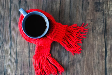 Blue cup with black tea, coffee or hot chocolate in  red scarf on brown wooden background. The concept of home comfort in cold season. Hugge.