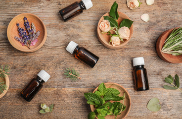 Different essential oils and ingredients on wooden background, flat lay