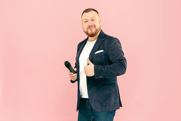 Young man with microphone on pink background, leading with microphone at studio concept. Human emotions and facial expressions concepts. Trendy colors