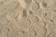 Sand On The Beach With Footprints And Shoes. Many Footprints With Shoes And Without Shoes.
