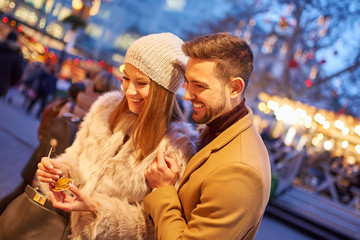 A beautiful young couple smiling and checking the gifts in a christmas market.