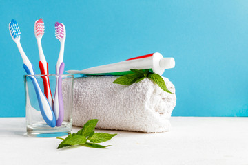 Wall Mural - Healthy teeth. Toothbrush in a glass and toothpaste and mint leaves a bath towel on the table in the bathroom on a blue background. Design, health care, hygiene health and fresh breath