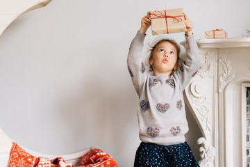 a little beautiful girl with modern clothes is on the background of a fireplace and a month decorate