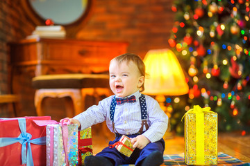 funny baby sitting on the floor near the gifts and having fun, on the background of the Christmas tree