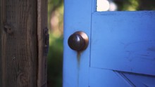 Slow-motion, Close-up Shot Of Blue Garden Door Opening With Emphasis On The Door Knob And A Soft Green Background.