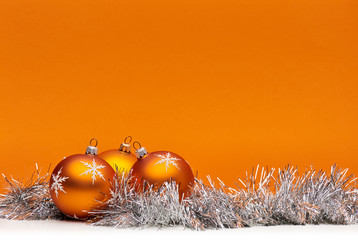 three orange bauble christmas decorations against an orange background with space for adding text.