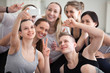 © fizkes - Group millennial positive laughing sportive athletic girls and guys at gym training studio. People smiling make peace sign symbol taking selfie photo feels happy and satisfied friendship unity concept