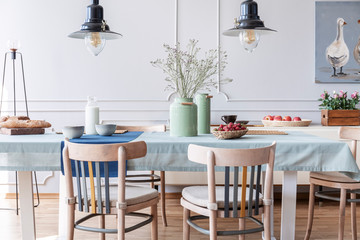 Wall Mural - Wooden chairs at table with flowers and food in white cottage dining room interior with lamps and poster. Real photo