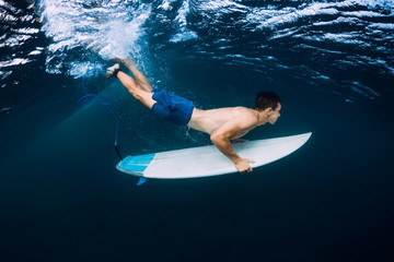 Professional surfer with surfboard dive underwater with ocean wave.