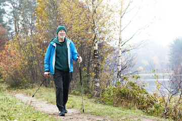 picture of active fit caucasian elderly man wearing sports clothes and warm hat having walk using no