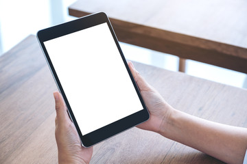 Mockup image of hands holding and using black tablet pc with blank white desktop screen while sitting in office