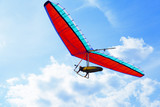 The hang glider on a red hang-glider is flying in a blue sky