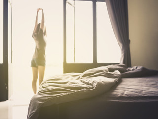 Confusion duvet and bed in luxury bedroom and healthy young woman stretching and relaxing by the window after waking up in the morning of holiday. Selective focus.