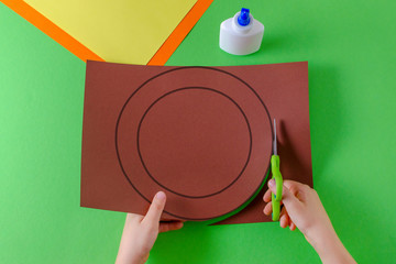 child's hands cut circle on brown paper with scissors, top view, on green