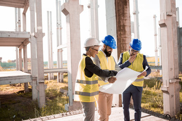 Canvas Print - A beautiful young female architect shows at the blueprints a new construction solution.