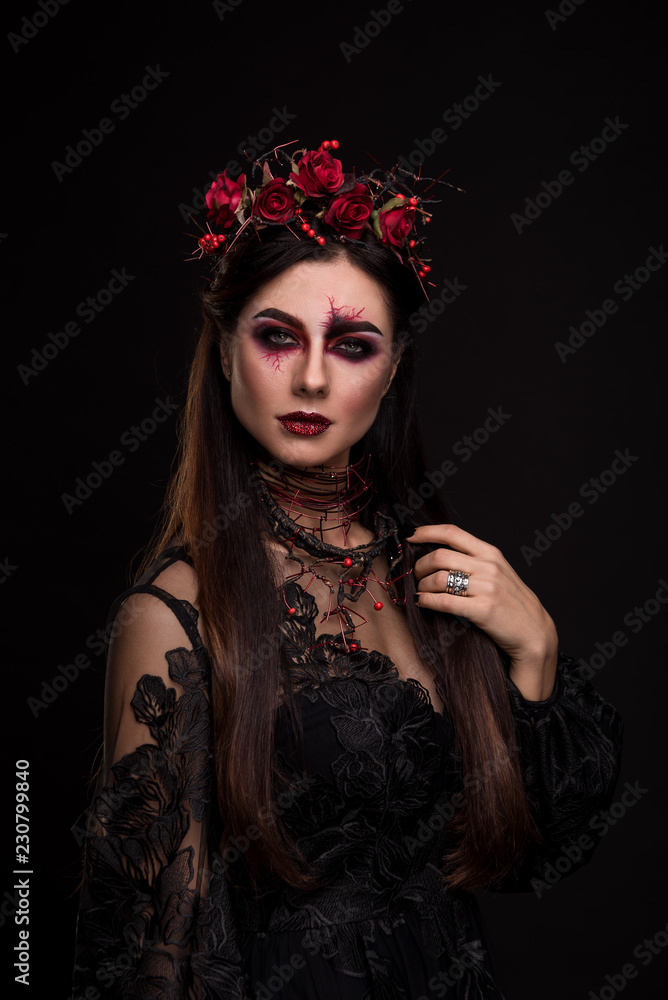 Photo Stock Portrait of a girl in the image for Halloween. Black Widow.  Wreath of roses. Makeup for halloween. Eyes like gimlets. Black lace dress.  Black background. | Adobe Stock
