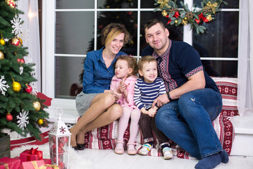 Happy family near christmas tree. Parents and two little children having fun and playing together near Christmas tree