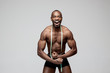 Fit young man with measuring tape isolated on gray background. The naked torso of African American man posing at studio. The muscular body, fitness, sports, healthy lifestyle and bodybuilder concept.