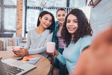 Wall Mural - Friendly relationships. Selfie of delighted young women sitting at the table while working together