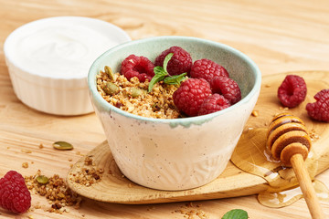 Wall Mural - Homemade granola and yogurt in a bowl with raspberries on a wooden table.