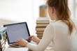 © fizkes - Close up woman student sitting at the desk typing writing message mail looking at computer with mock up blank screen, view over the shoulder. Girl with heaps stack of books studying at home or library
