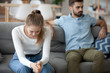 © fizkes - Unhappy young millennial married couple sitting on couch in living room after quarrel fight. Angry husband frustrated offended wife at home. Break up, divorce and misunderstanding in relations concept