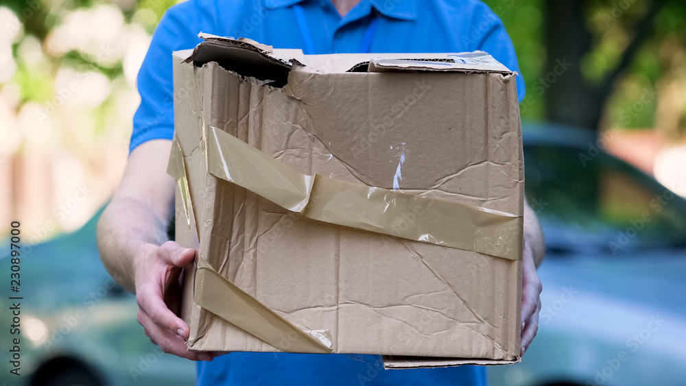 Male courier showing damaged box, cheap parcel delivery, poor shipment quality - obrazy, fototapety, plakaty 