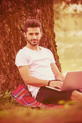 man using a laptop computer on the bank of the river