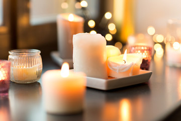 hygge, decoration and christmas concept - candles burning in lanterns and festive garland on window sill at home