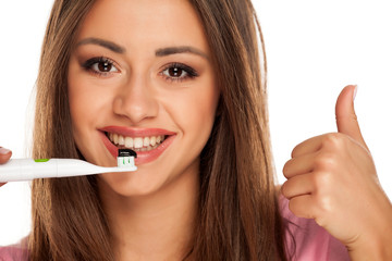 young woman holding electric tooth brush with black active charcoal toothpaste on white background and showing thunbs up