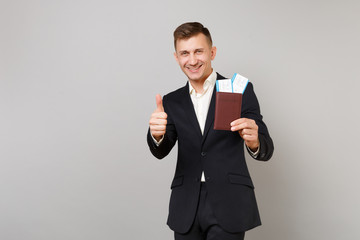 Joyful young business man in classic suit showing thumb up, holding passport, boarding pass ticket in hand isolated on grey background. Achievement career wealth business concept. Mock up copy space.