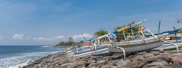 Wall Mural - Panorama of traditional Balinese fishing boats on the rocky beach of Balai Gili on Bali, Indonesia