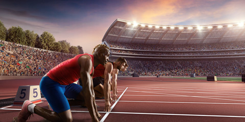 Wall Mural - Male athletes sprinting. Three men in sport clothes on starting line prepares to run at the running track in professional stadium