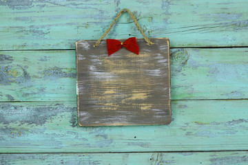 Wall Mural - Blank wood sign with red Christmas bow hanging on antique rustic teal blue wooden door; holiday background with painted copy space