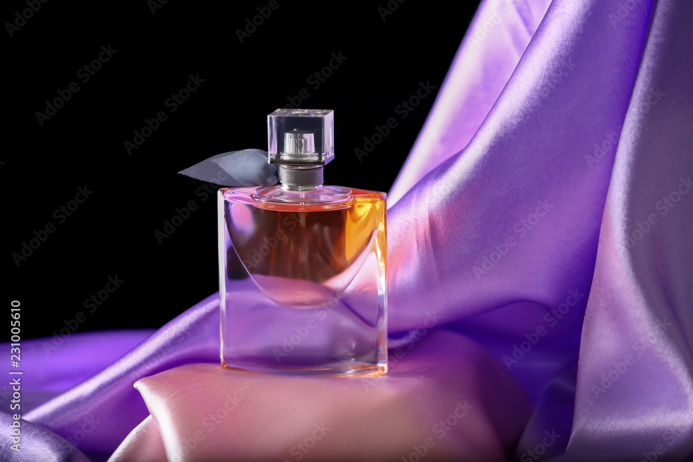 Bottle of perfume with shiny fabric on dark background