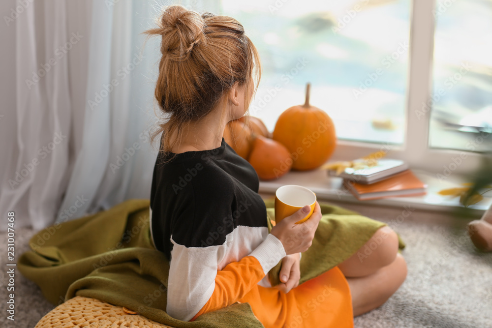 Woman drinking tea while resting at home on autumn day