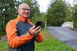 Happy Senior Man Thinking While Using Phone On The Side Of The Road