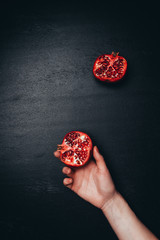 Wall Mural - partial view of female hand and cut pomegranate on black tabletop