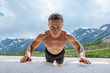 Front portrait of determined young sporty handsome man training topless on white sand, performing push-ups over beautiful mountain landscape background. Summer workout concept
