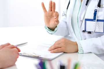 Doctor showing Ok sign to patient while sitting at the desk in hospital office, closeup of human hands. Medicine and health care concept