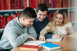 © Aleksandr - University students sitting together at the table with books and laptop. Happy young people doing group study in library