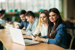 © Aleksandr - Group of college students studying in the school library, a girl and a boy are using a laptop and connecting to internet. Girl to the camera