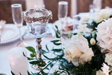 Wedding Table Serivce. Candles On Silver Vases And Glasses With Water Stand Among White Flowers On Wedding Dinner Table