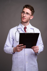 Young handsome man doctor wearing eyeglasses against gray backgr