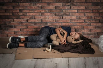 poor homeless boy sleeping with his toy on floor near brick wall