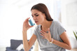 Young woman with asthma inhaler in light room