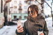 © bedya - Pretty girl walking on the street with phone and hot drink.