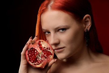 Wall Mural - portrait of a young girl with red hair and pomegranate fruit in hands on red background