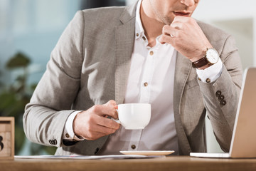 Poster - cropped shot of businessman with cup of coffee looking at laptop screen at office