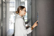 © rh2010 - Young business woman in white suit entering code on the intercom keyboard of the residential modern building